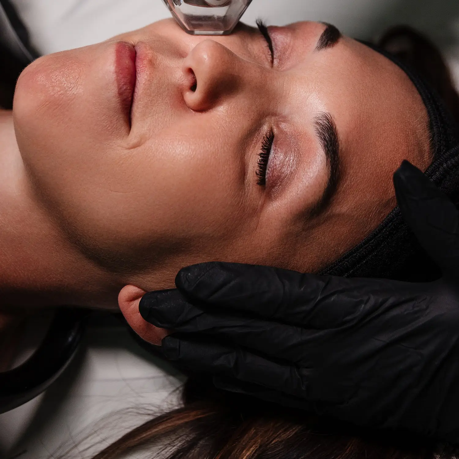 Client resting with eyes closed while a gloved provider passes the Tixel skin rejuvenation tip over her cheek and forehead